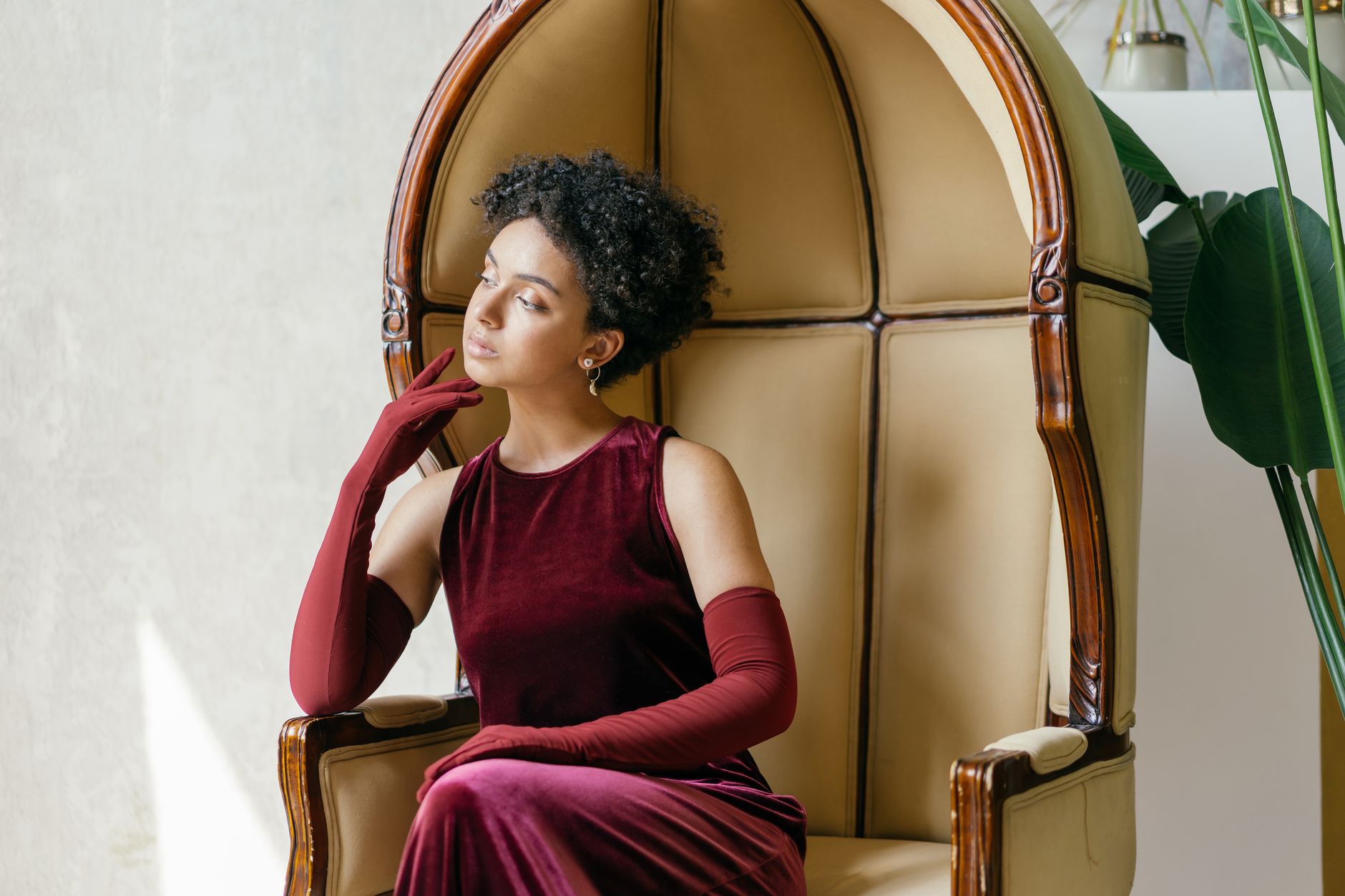 A stylish woman in a maroon velvet dress sitting in an armchair, exuding elegance.