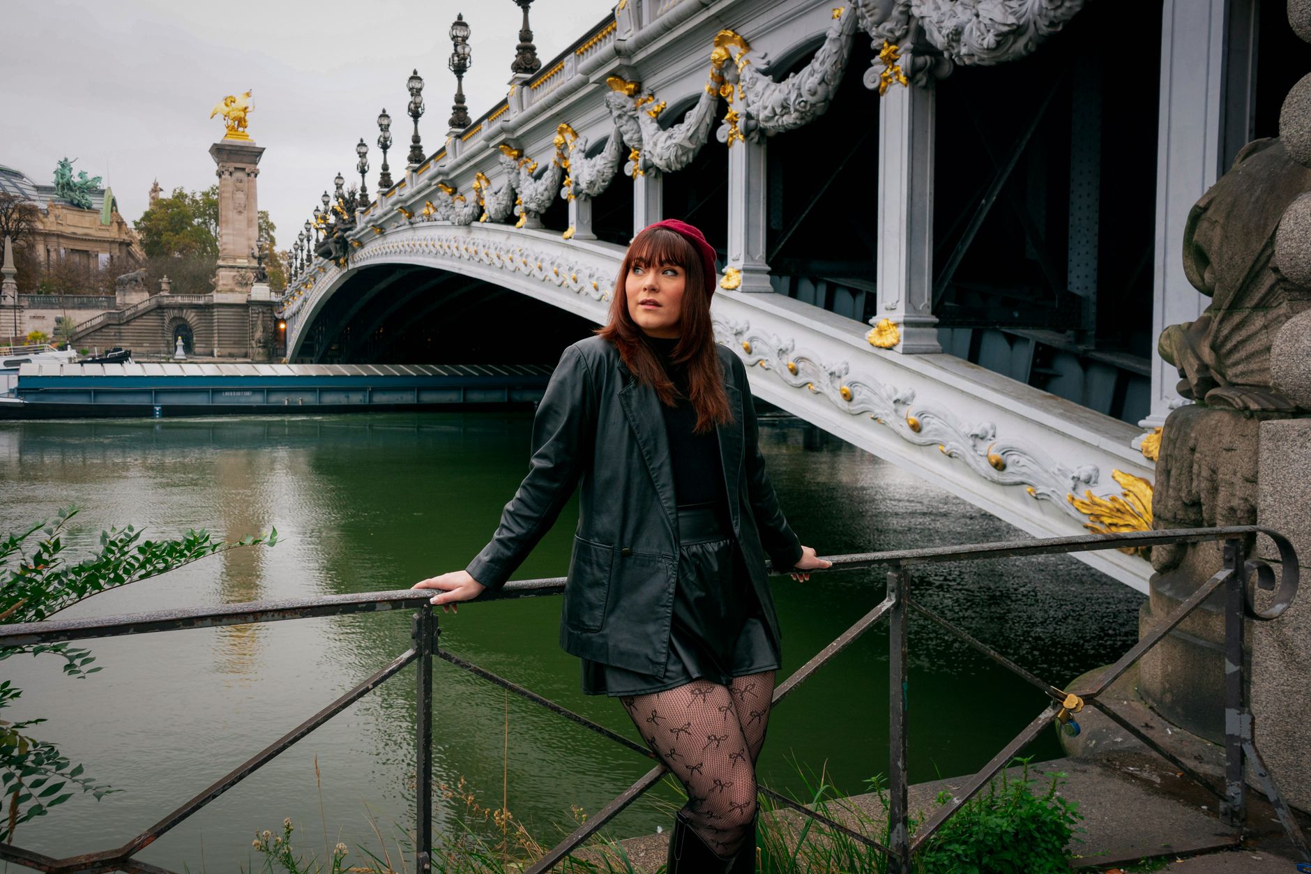 A stylish woman poses by Pont Alexandre III showcasing Parisian fashion in autumn.