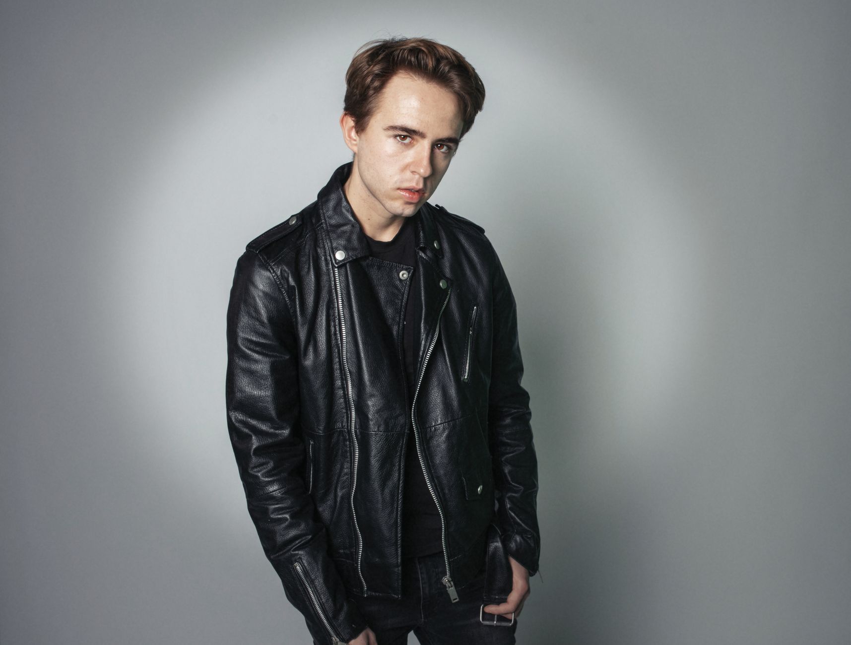 Portrait of a young man in a stylish black leather jacket on a gray backdrop.
