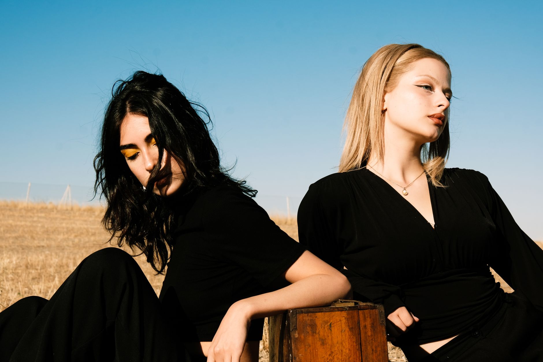Two fashion models in black blouses pose outdoors under a clear blue sky.
