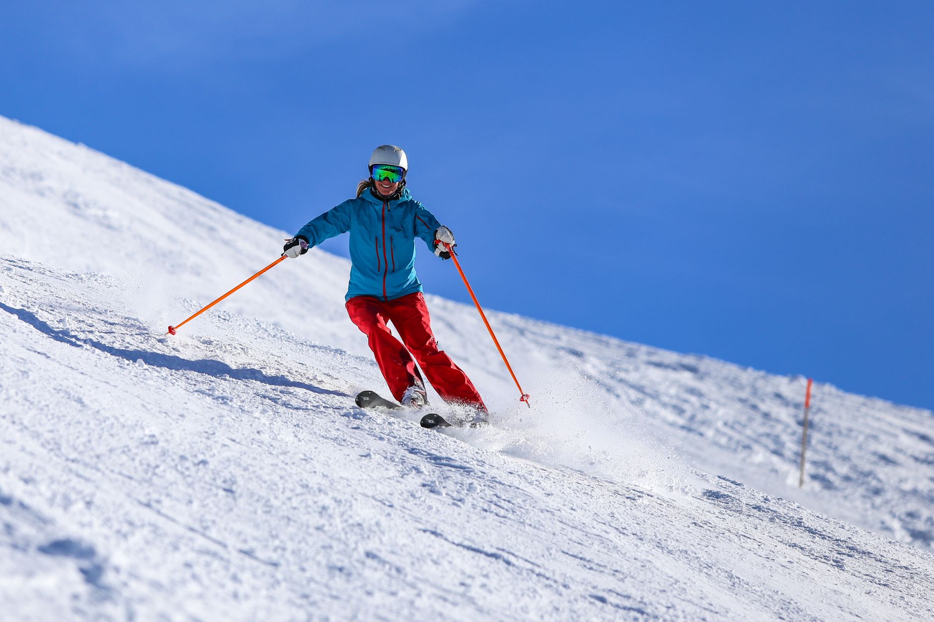 An adult skier in blue and red gear skiing down a snowy slope under a clear blue sky.