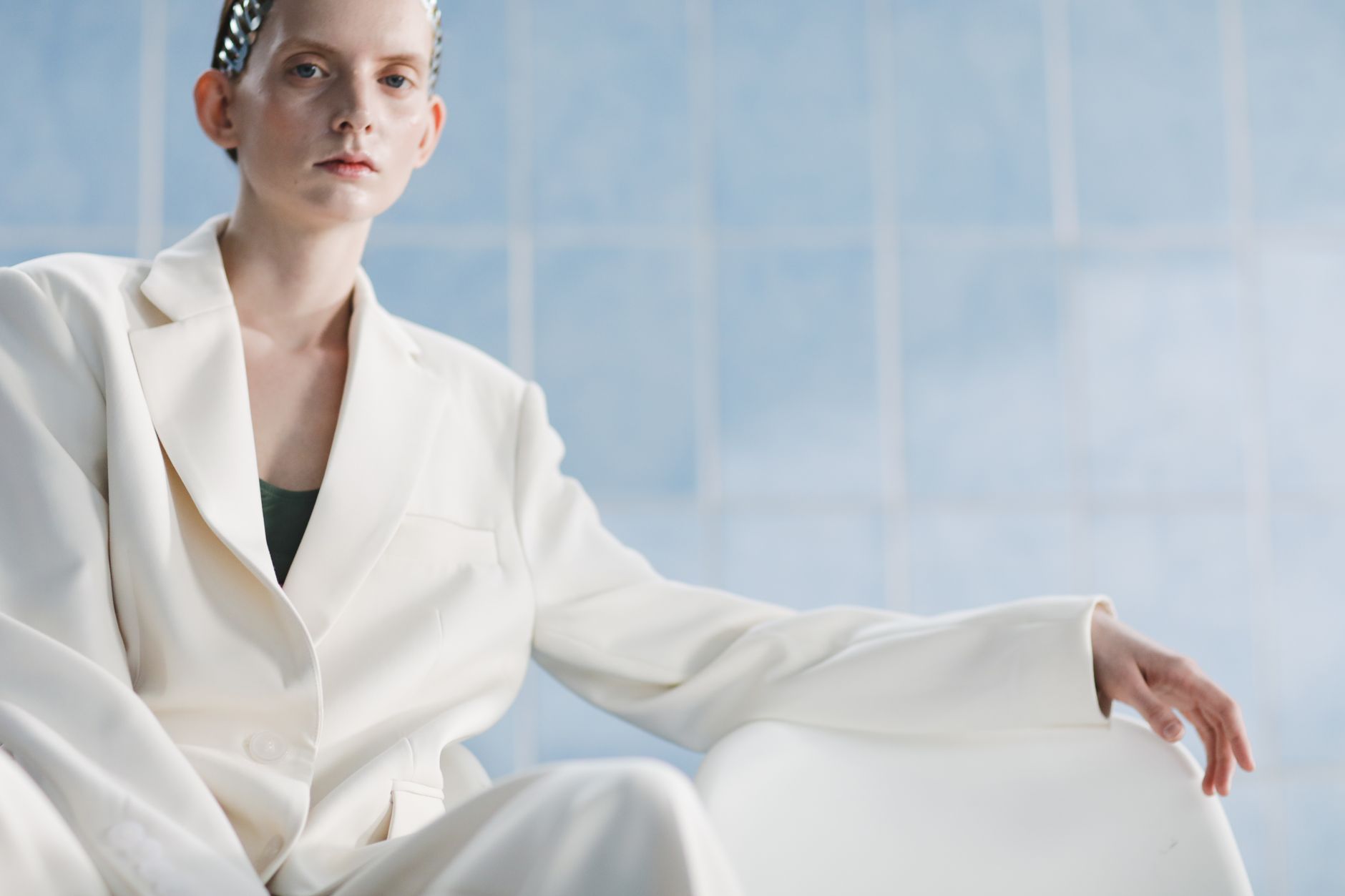 Stylish portrait of a woman in a white suit set against a minimalist blue background.