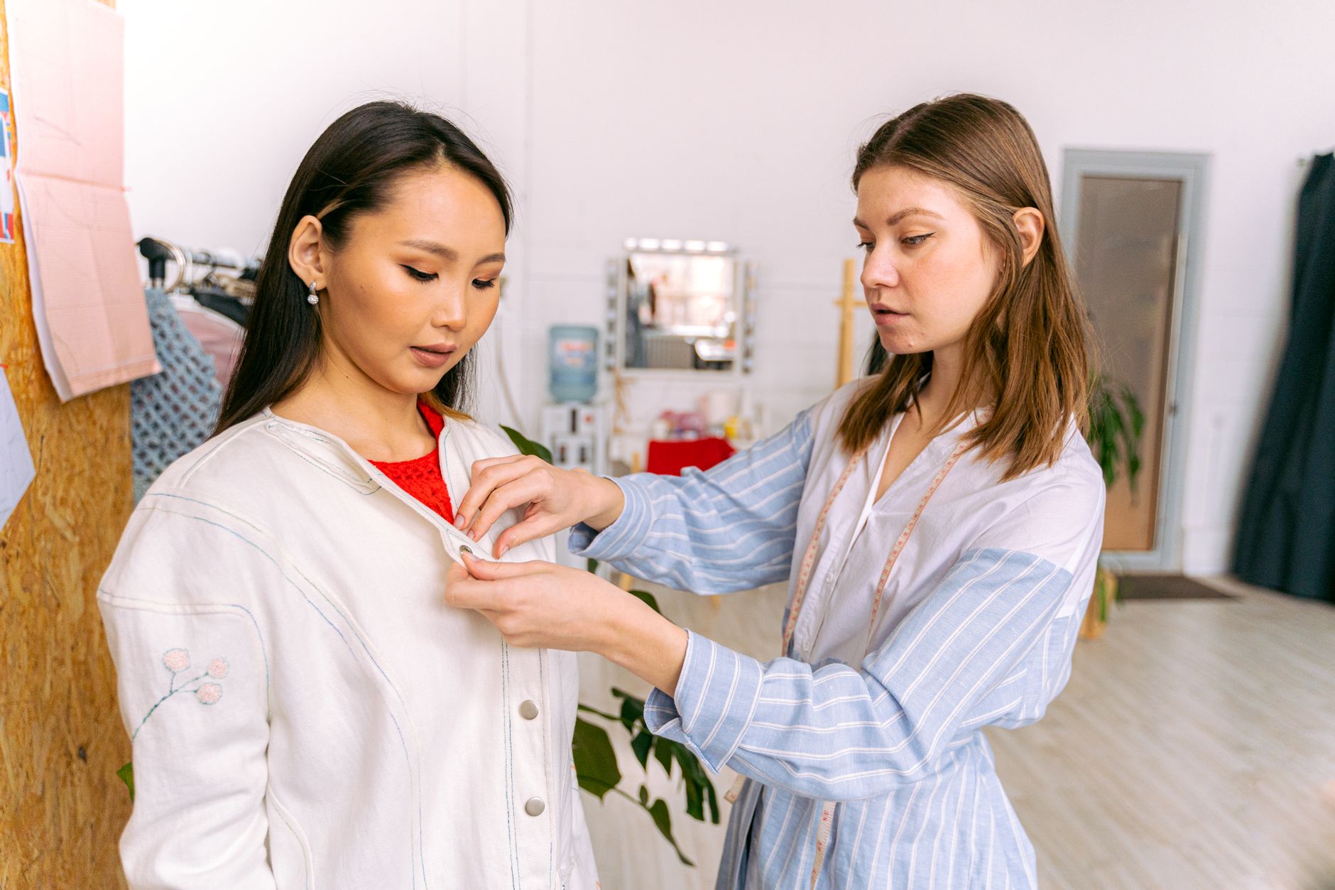 A fashion designer adjusting a garment on a model in a modern studio setting.